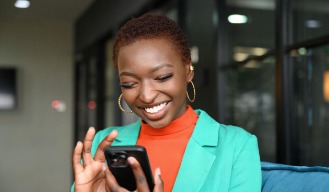 A young woman smiling at her phone while banking on the go